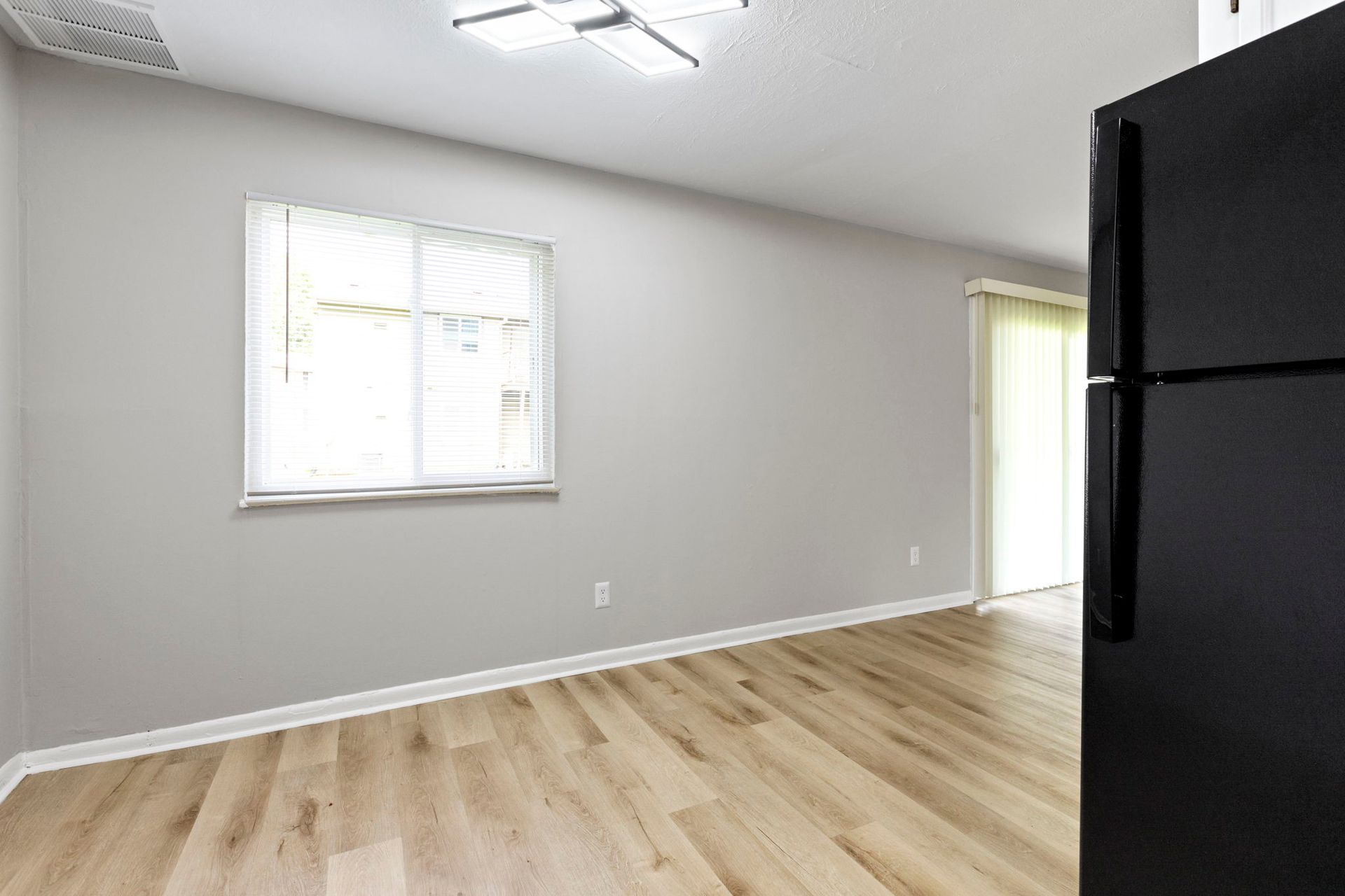 Empty room with light wood floors, gray walls, and a black refrigerator.