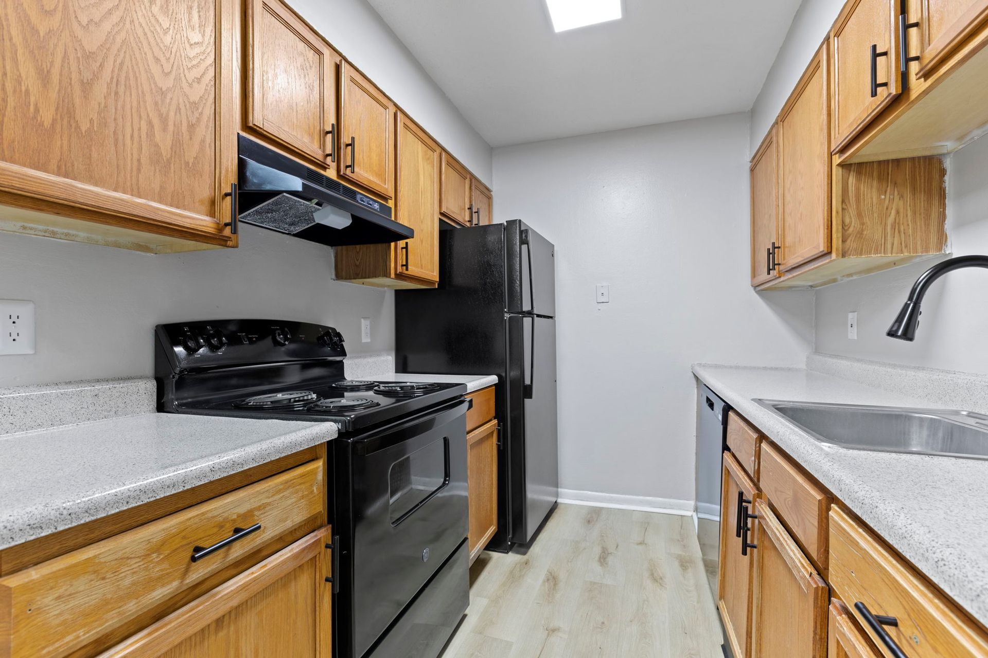 Kitchen with light wood cabinets, black appliances, and light gray countertops.