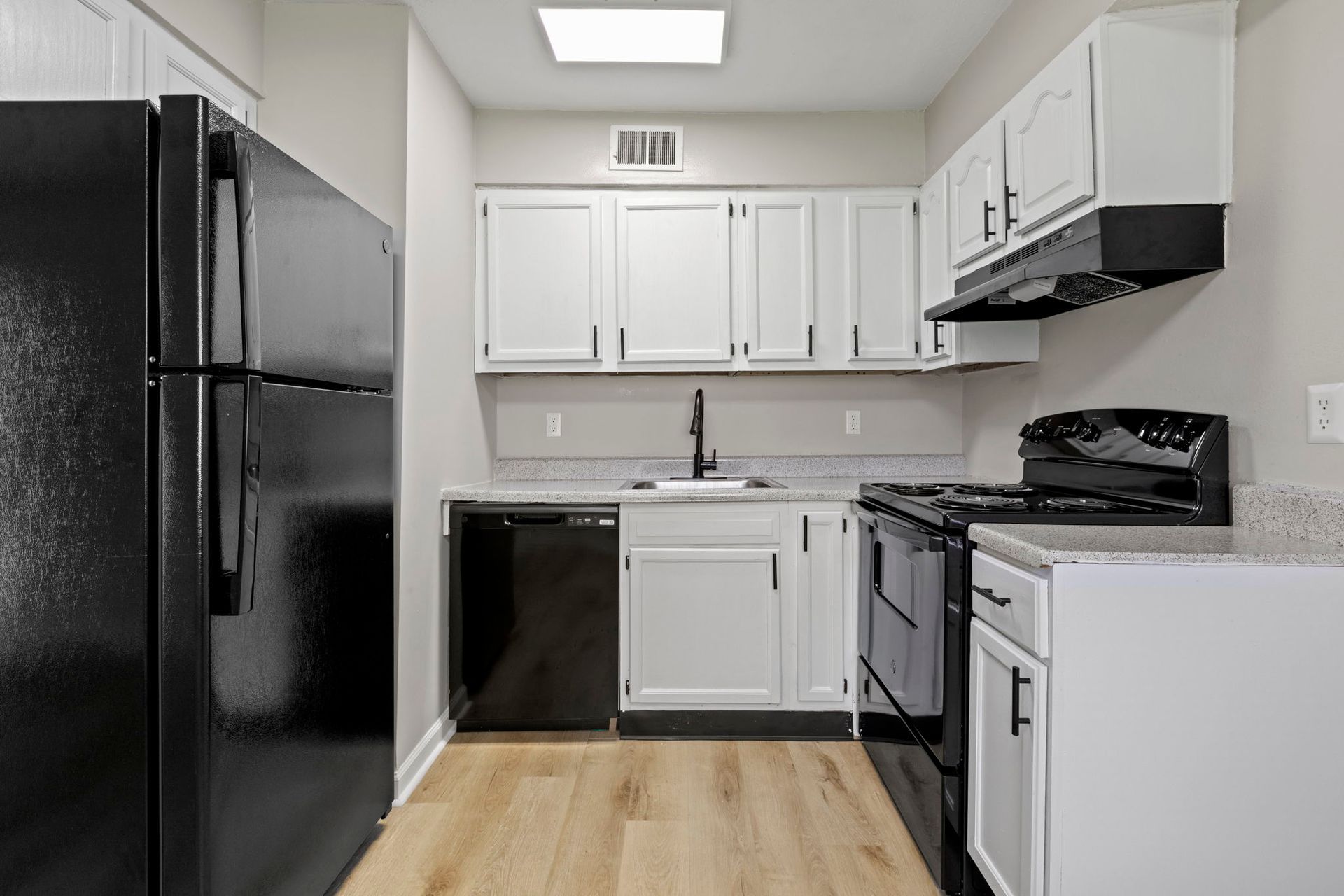 Kitchen with black appliances, white cabinets, and light-colored flooring.