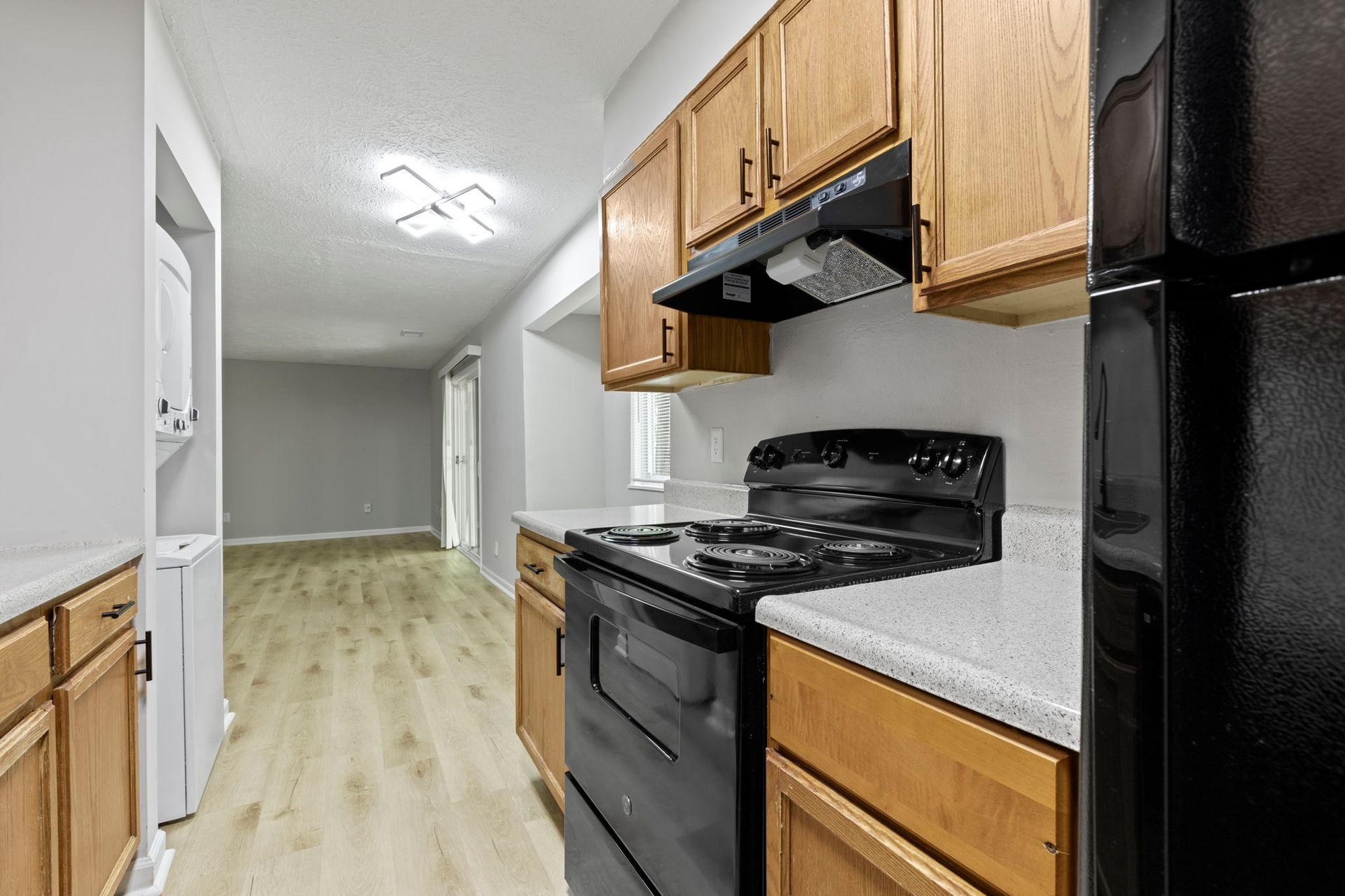 Kitchen with wooden cabinets, black appliances, and light countertops. A view into the living area.