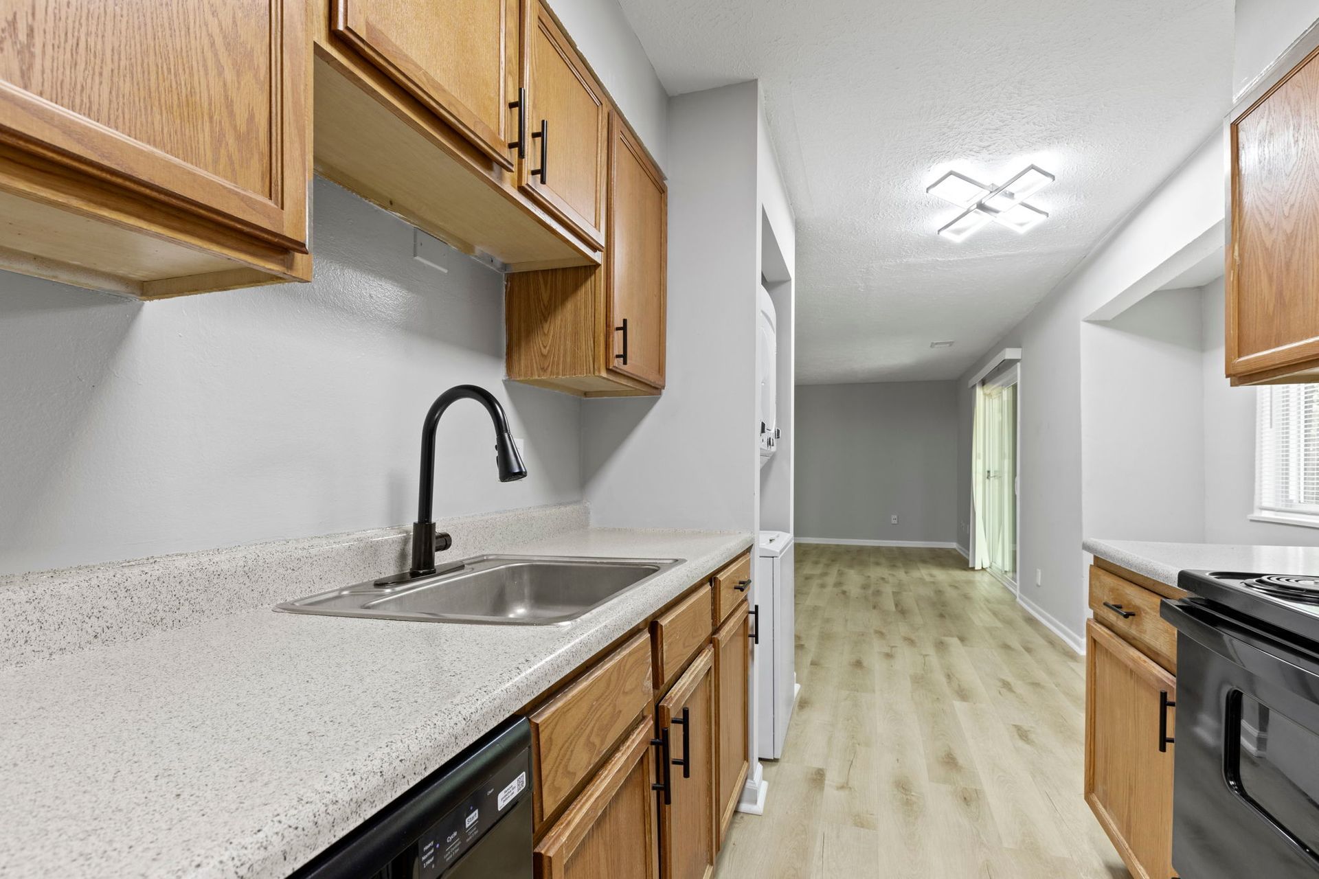 Kitchen with light wood cabinets, light countertops, black faucet and appliances, and a view into a living room.