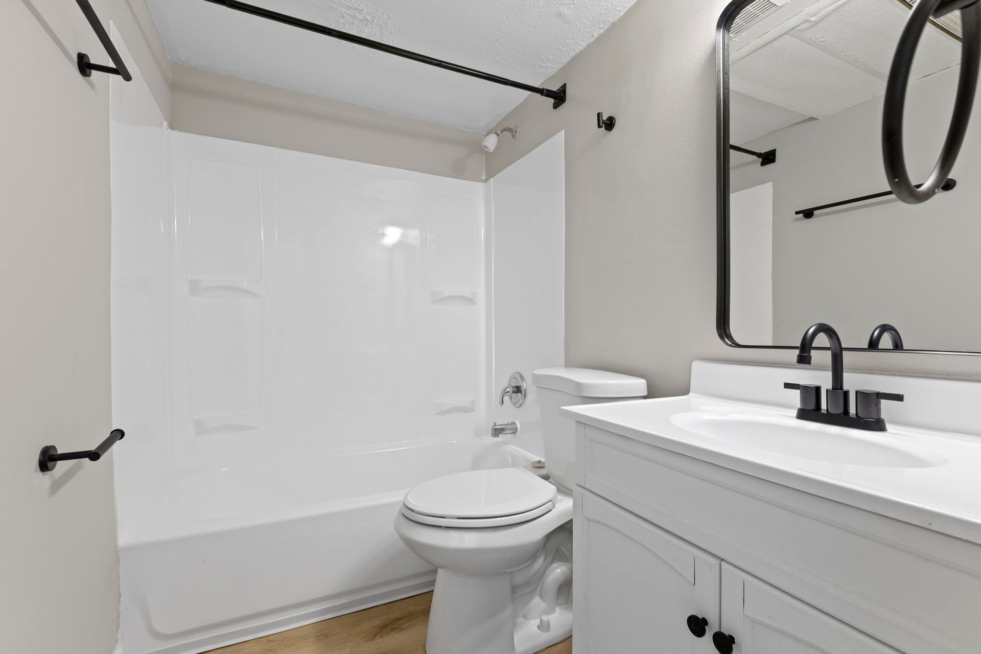 White bathroom with a tub, toilet, and vanity with black fixtures.