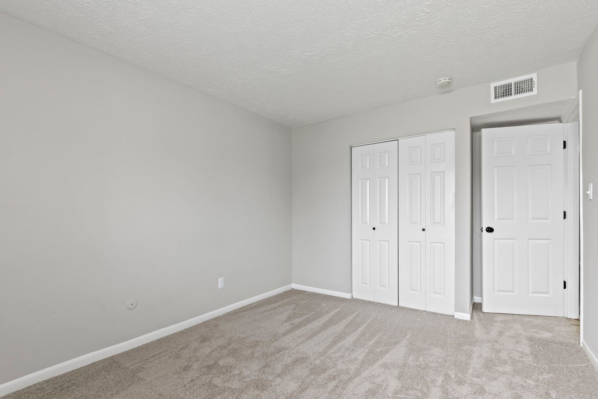 Empty bedroom with gray carpet and walls, white closet and door.