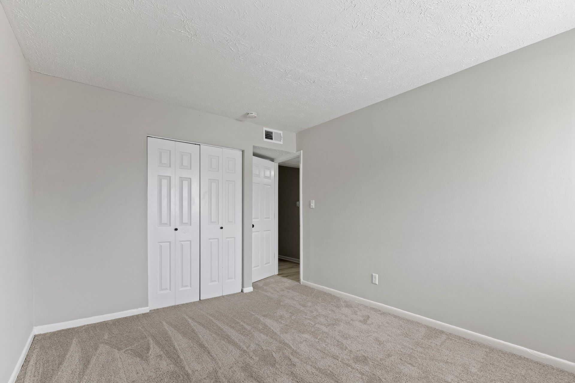 Empty bedroom with gray walls, white bi-fold closet doors, and beige carpet.