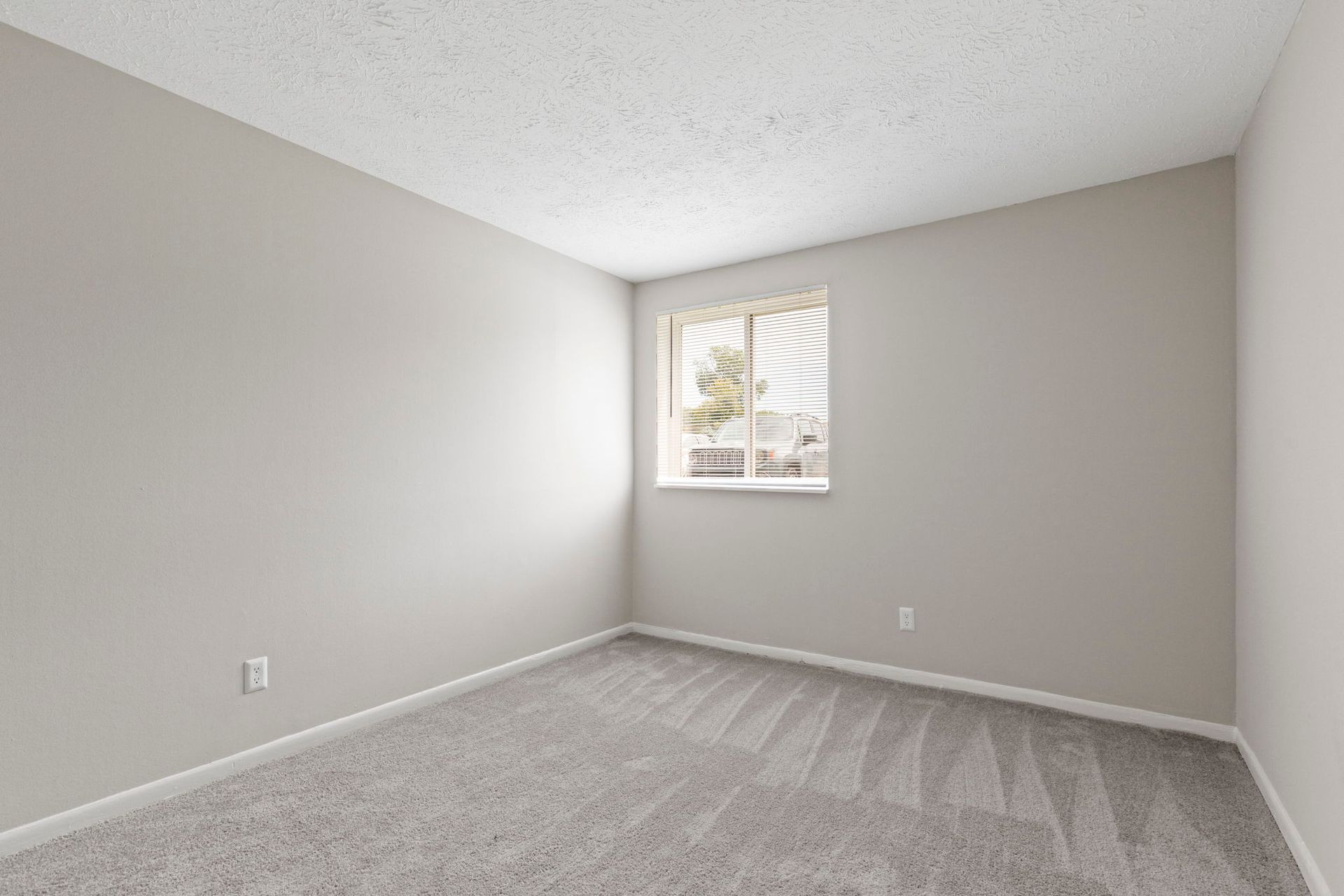 Empty room with gray walls, carpet, and a window with blinds.