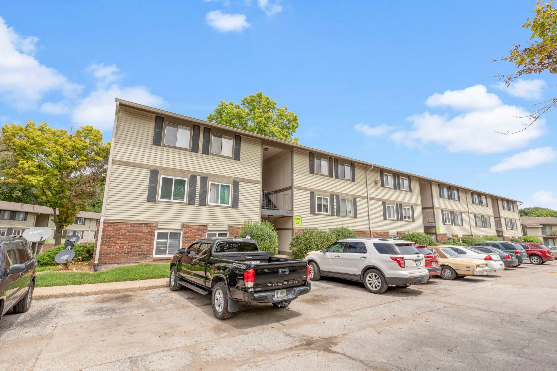 Two-story apartment building with parked cars in front on a sunny day.