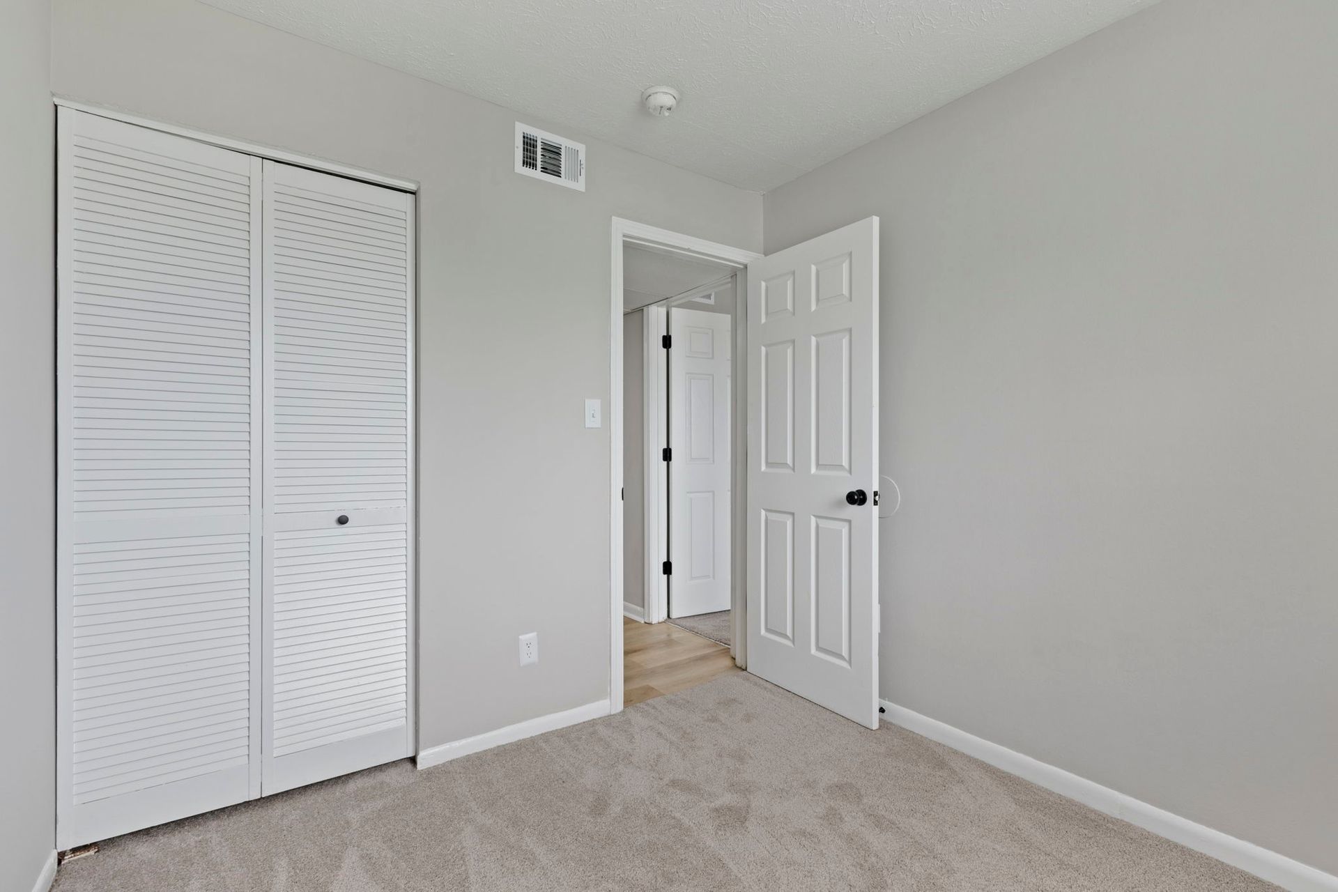 Empty bedroom with gray walls, a carpet, a closed wardrobe, and a doorway to another room.