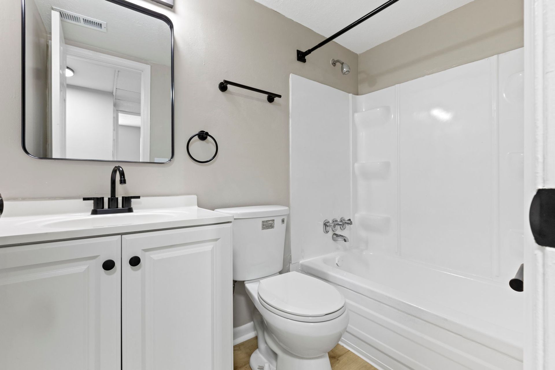 Bathroom with white vanity, toilet, and tub, black fixtures, and a mirror.