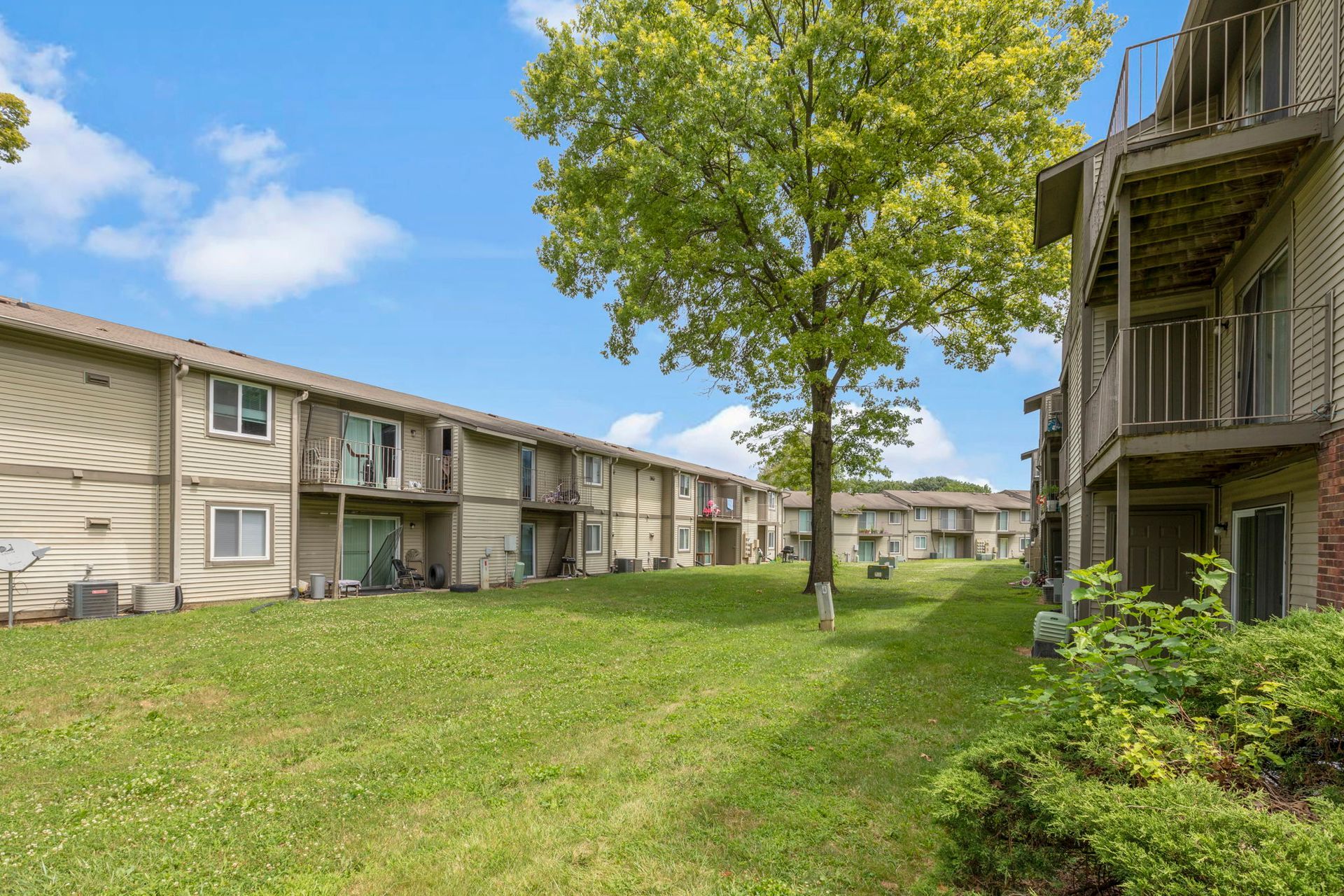 Apartment complex with tan siding, green grass, and a blue sky with clouds.
