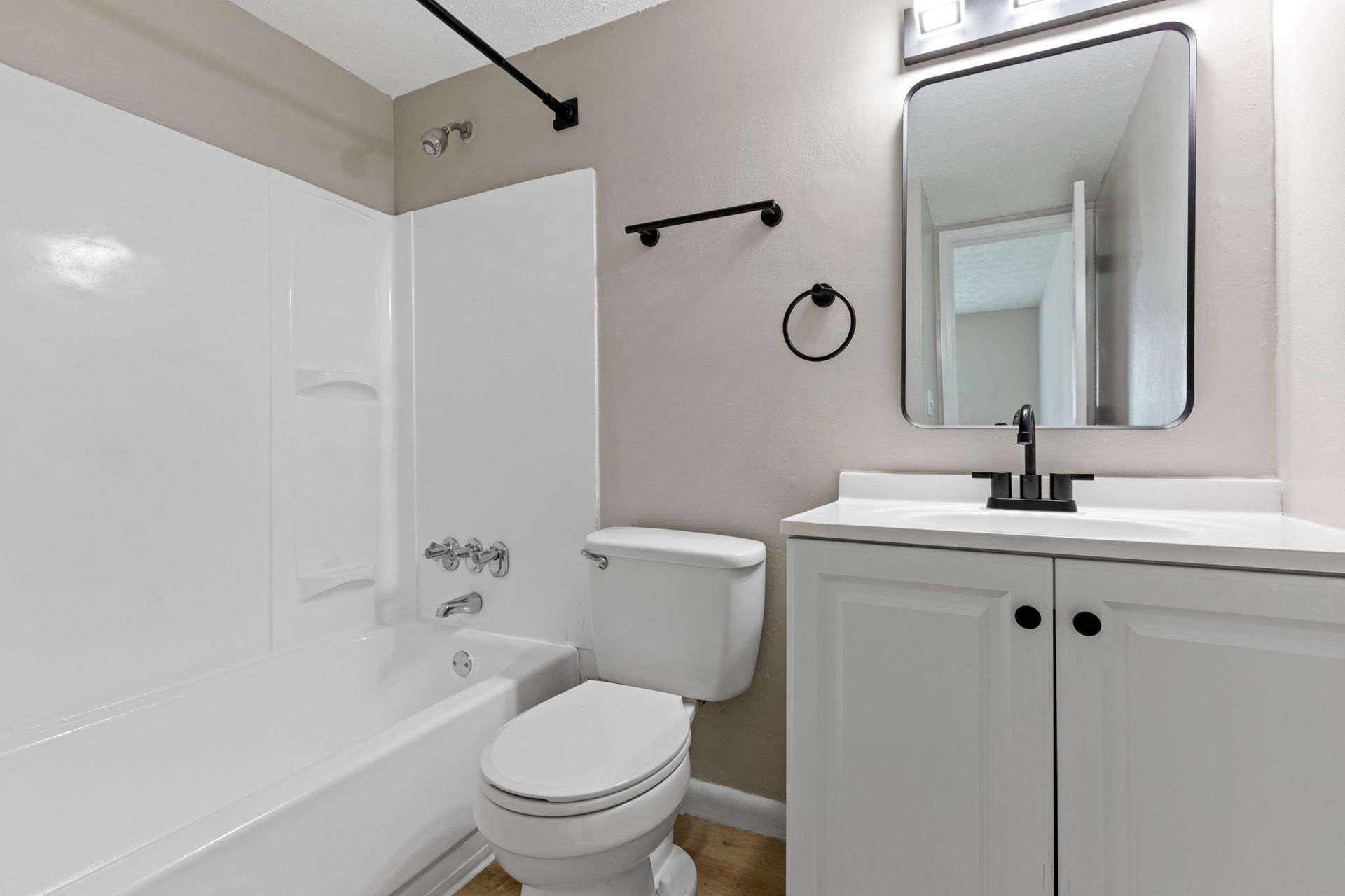White bathroom with bathtub, toilet, vanity, and black fixtures.
