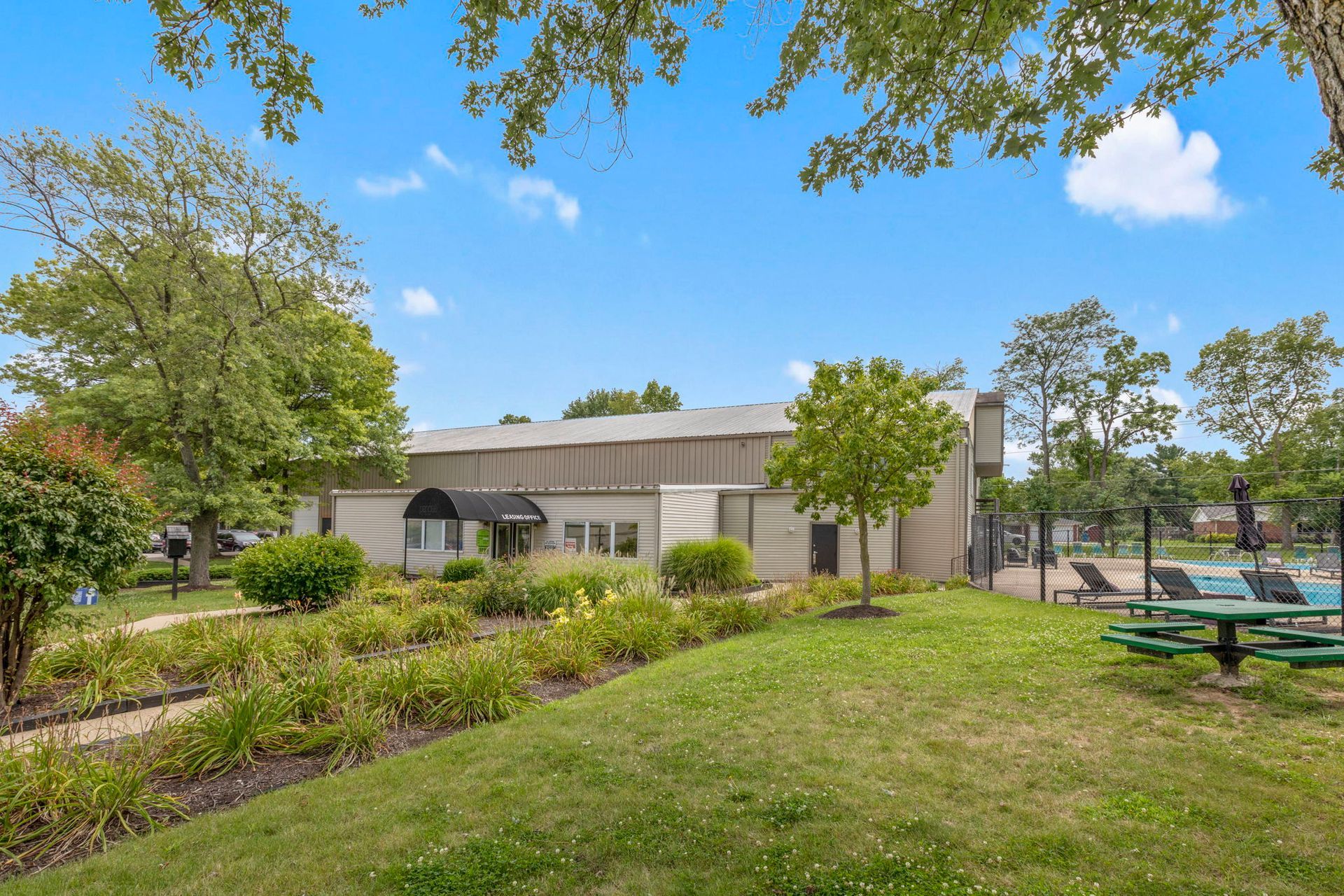 A building with a black awning, set in a green grassy area with trees and a pool in the background.
