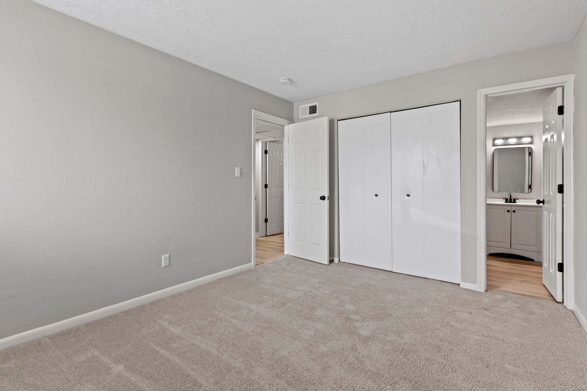 Empty bedroom with gray walls, carpet, white doors, and a bathroom doorway.