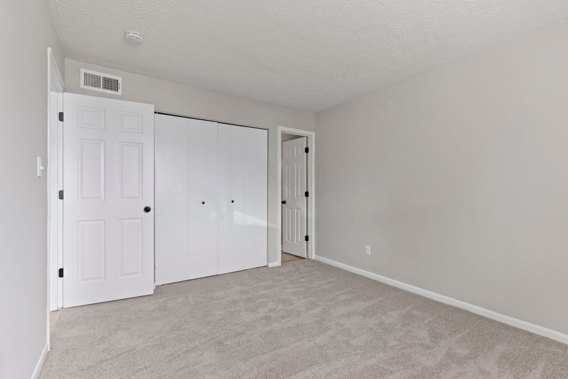 Empty bedroom with light gray walls, white doors, and beige carpet.