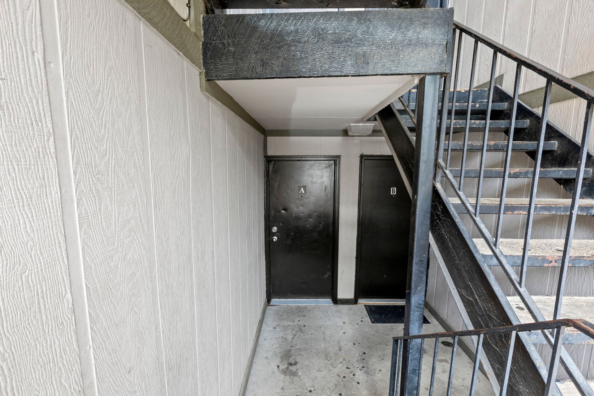 Apartment hallway with two black doors, stairs, and textured white walls.
