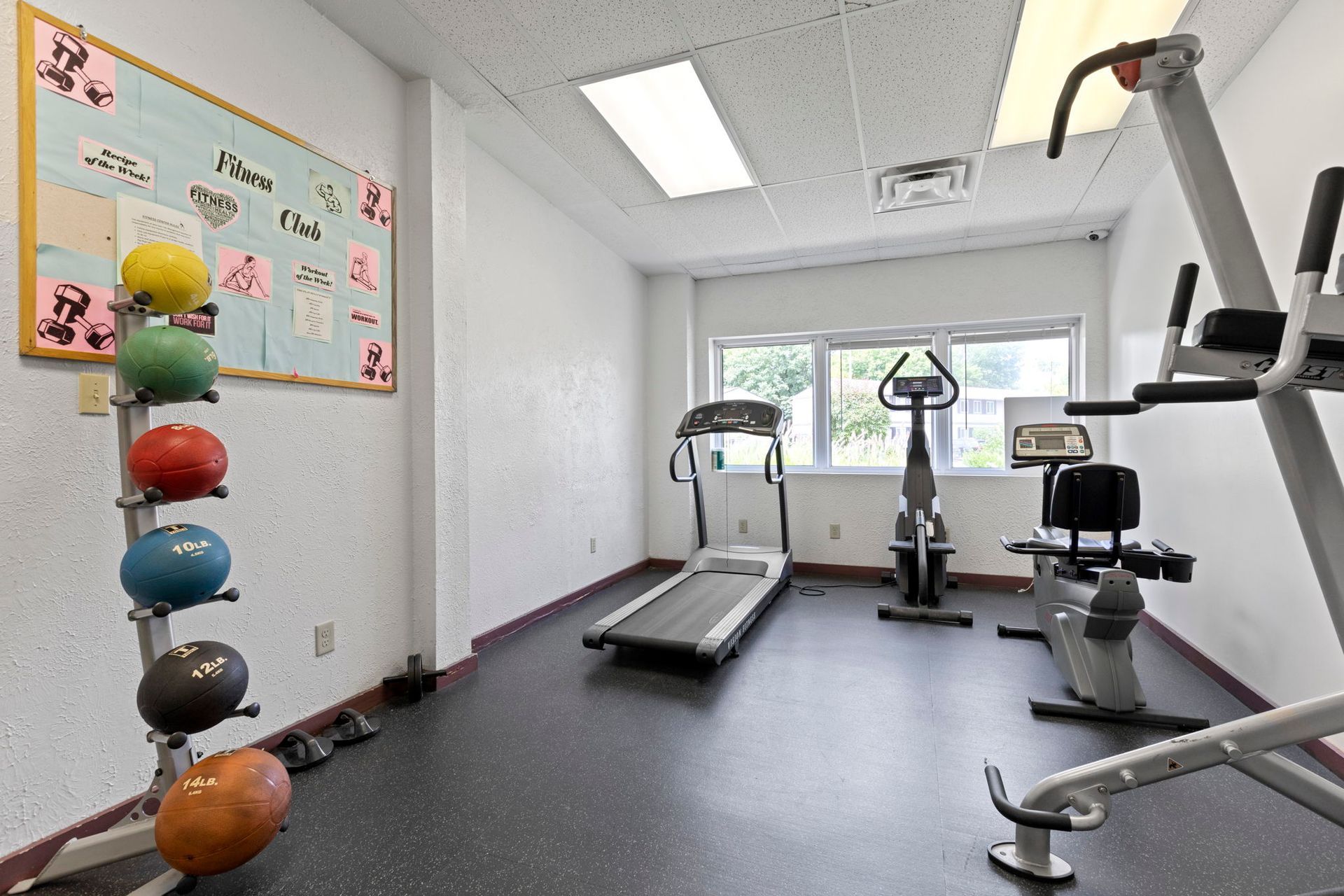 Small gym with exercise equipment: treadmill, stationary bike, and weights.