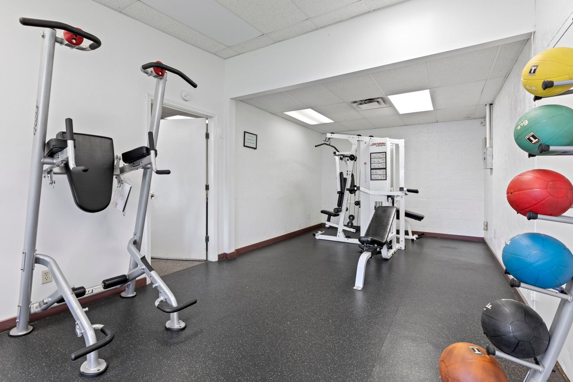 Gym with weight machines, medicine balls, and inversion machine on a black floor.