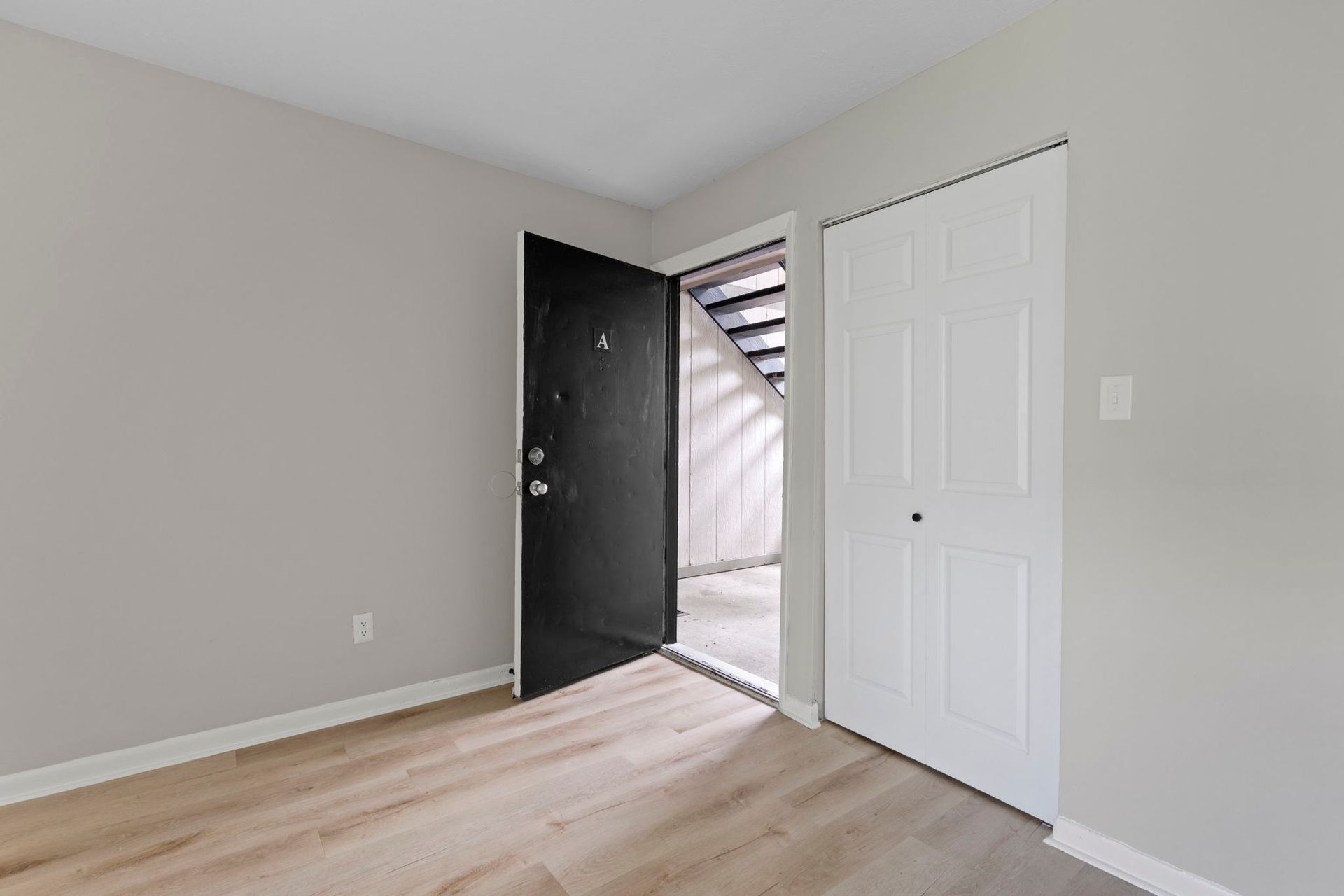 Interior room with open black door, white closet, and light wood floors. Gray walls.