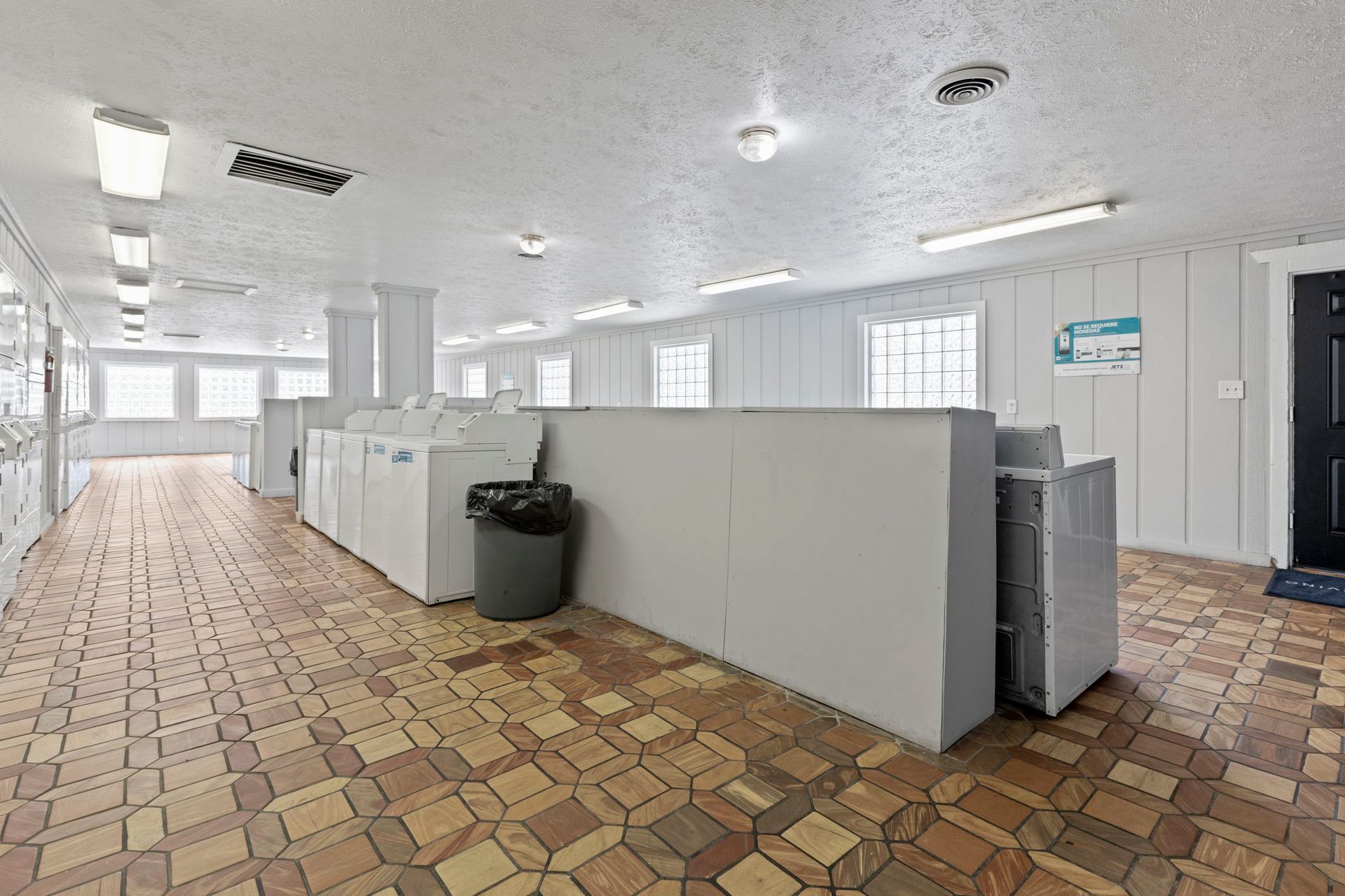 Laundry room with rows of white washing machines, tan floor, and fluorescent lighting.