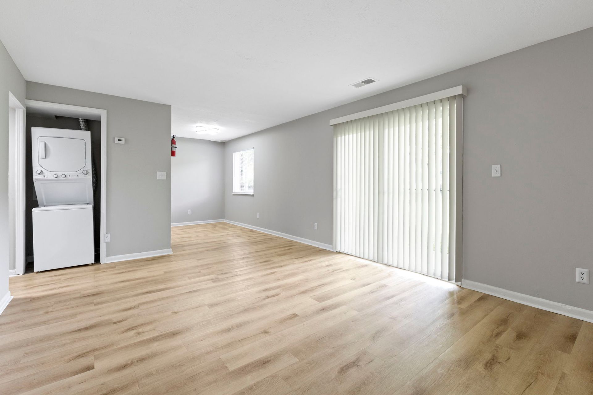 Empty living room with wood floors, gray walls, sliding glass door, and laundry closet.