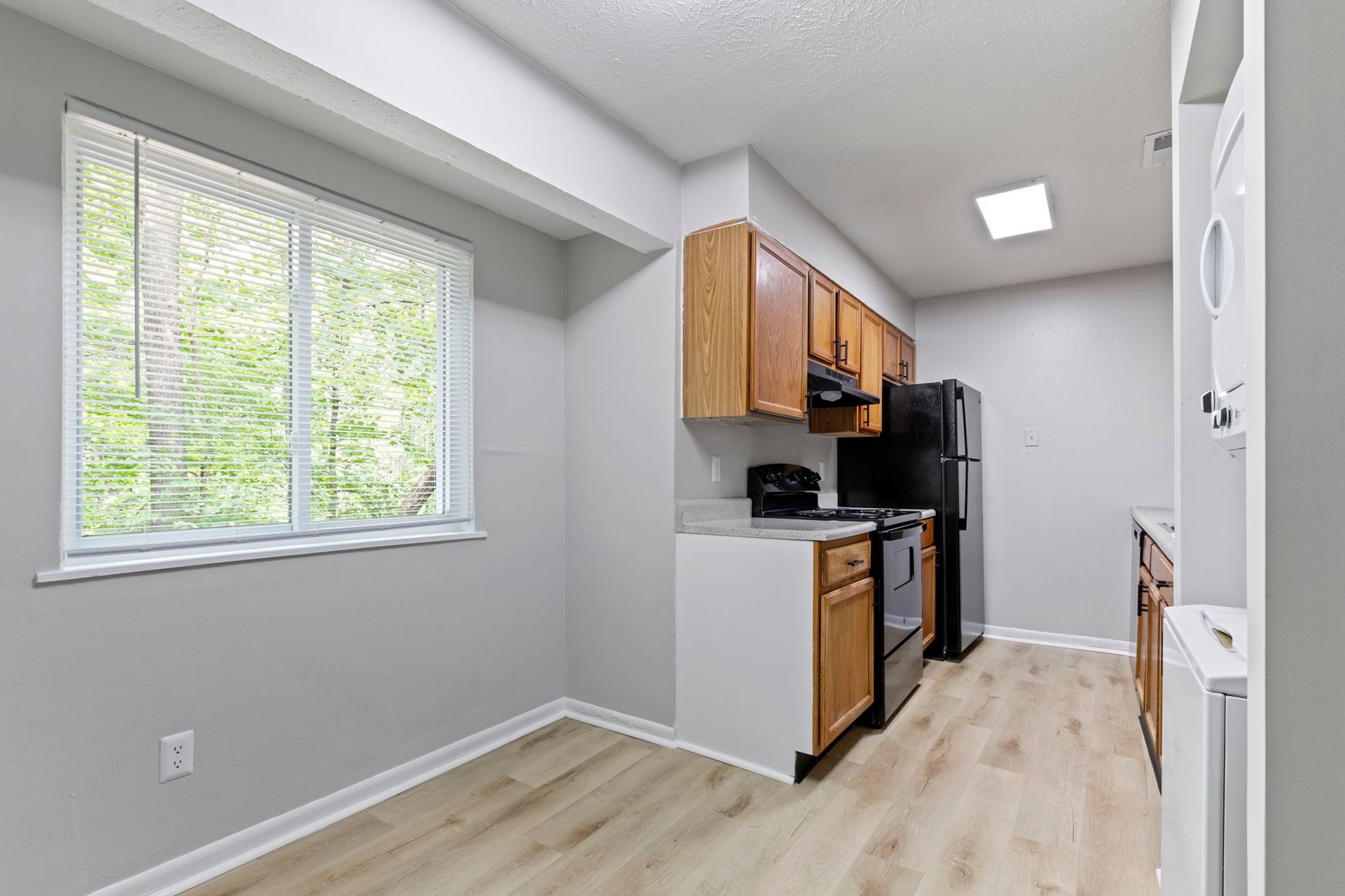 Kitchen with light wood floors, wood cabinets, black appliances, and a window.