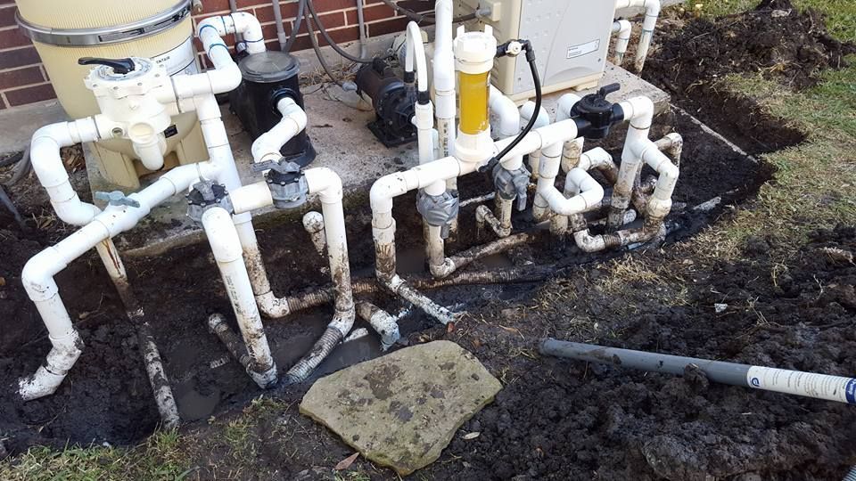 A bunch of pipes are laying in the dirt on the ground.