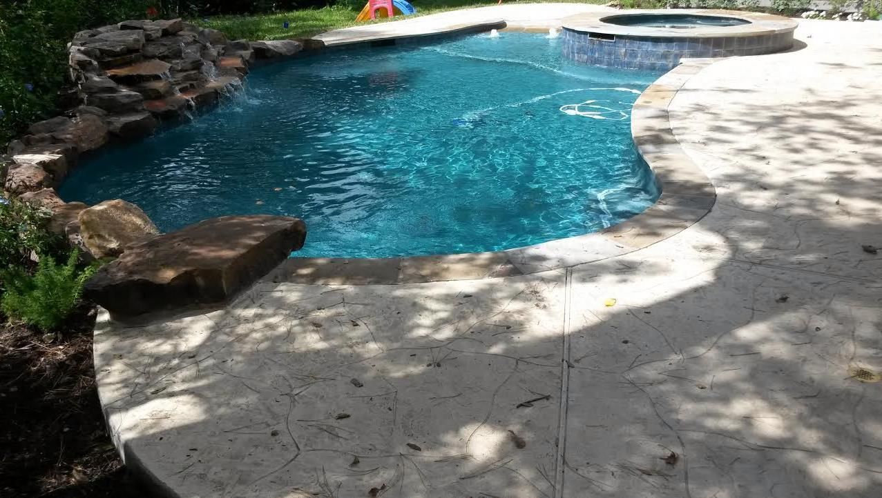 A large swimming pool with a hot tub in the backyard.