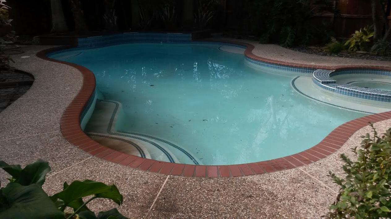A large swimming pool with a hot tub in the backyard at night.