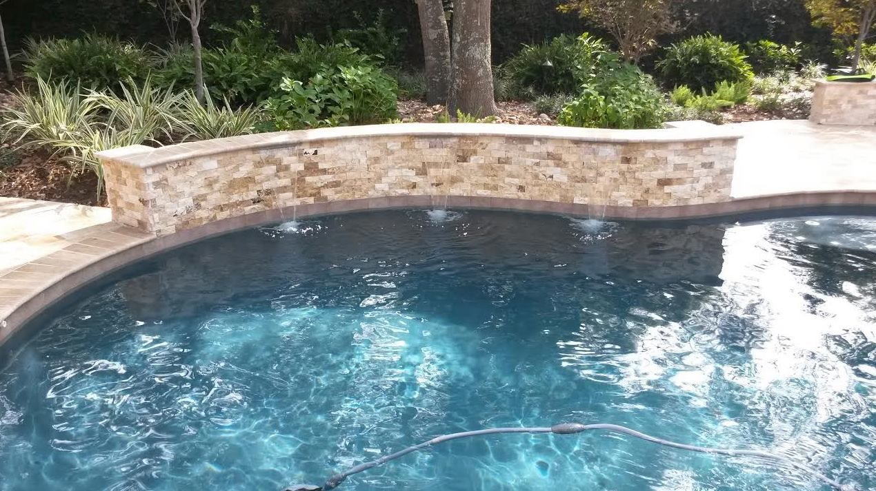 A large swimming pool with a stone wall surrounding it.