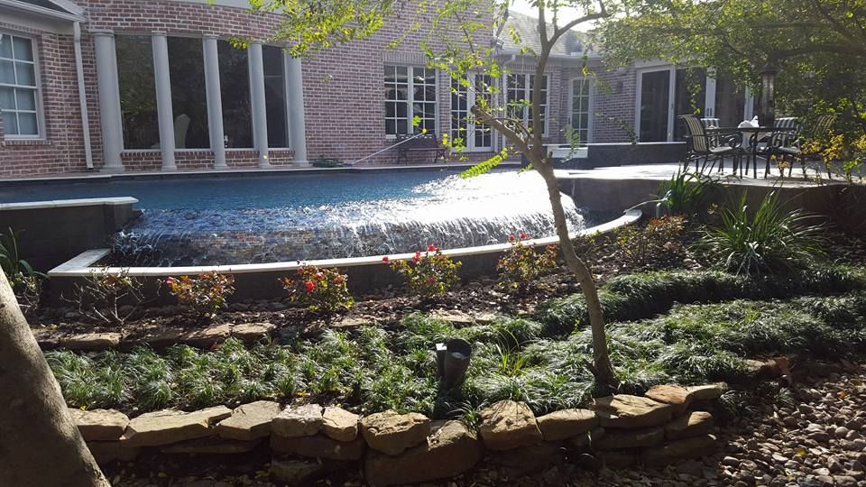 A large swimming pool with a waterfall in the backyard of a house.