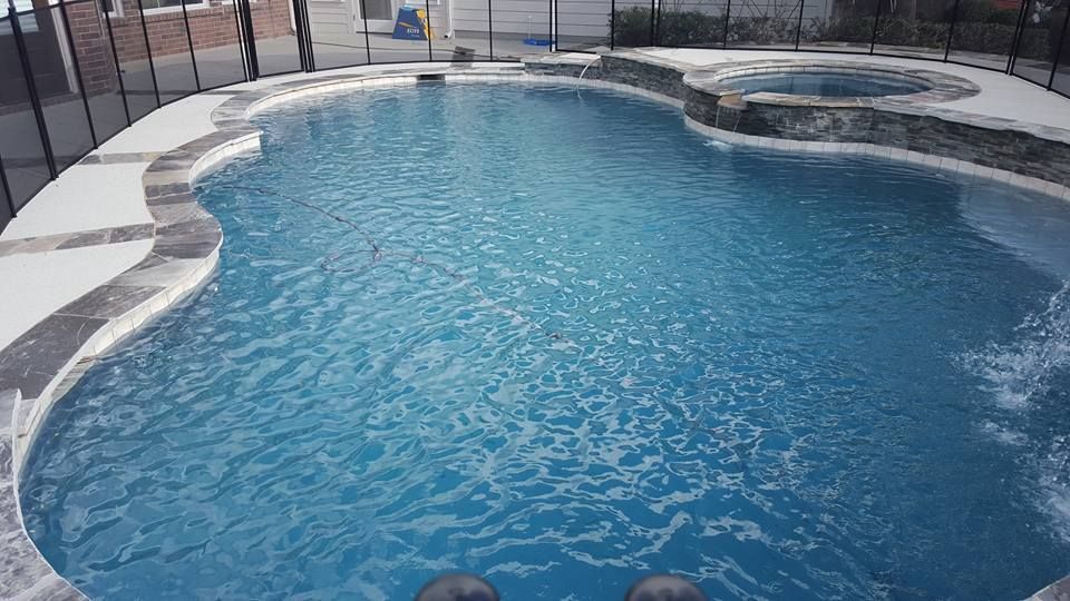 A large swimming pool with a hot tub in the backyard.