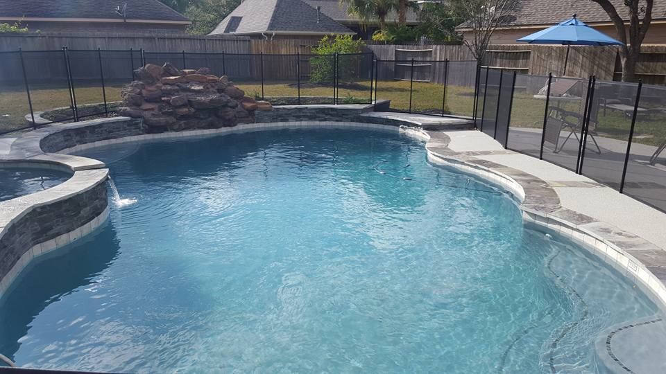 A large swimming pool with a fence around it and a blue umbrella.