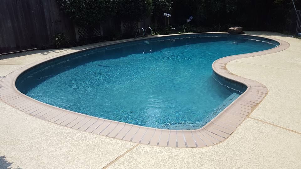 A large swimming pool with a brick border and a fence in the background.