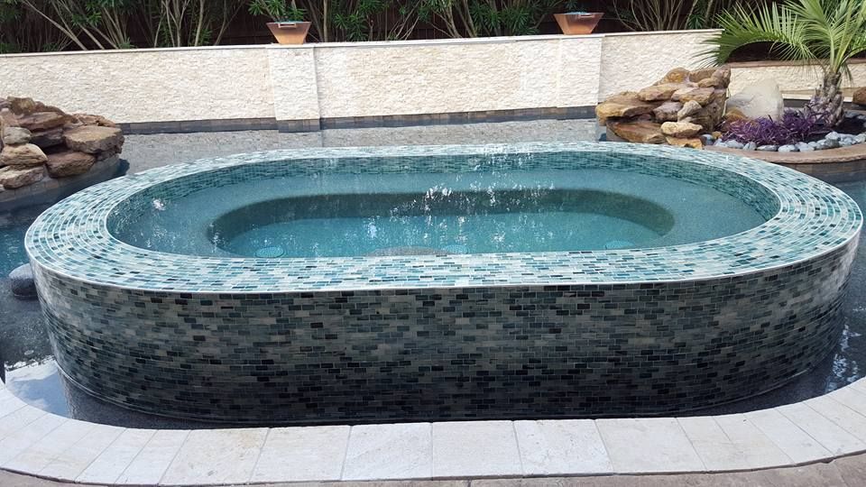 A large oval hot tub is sitting next to a swimming pool.