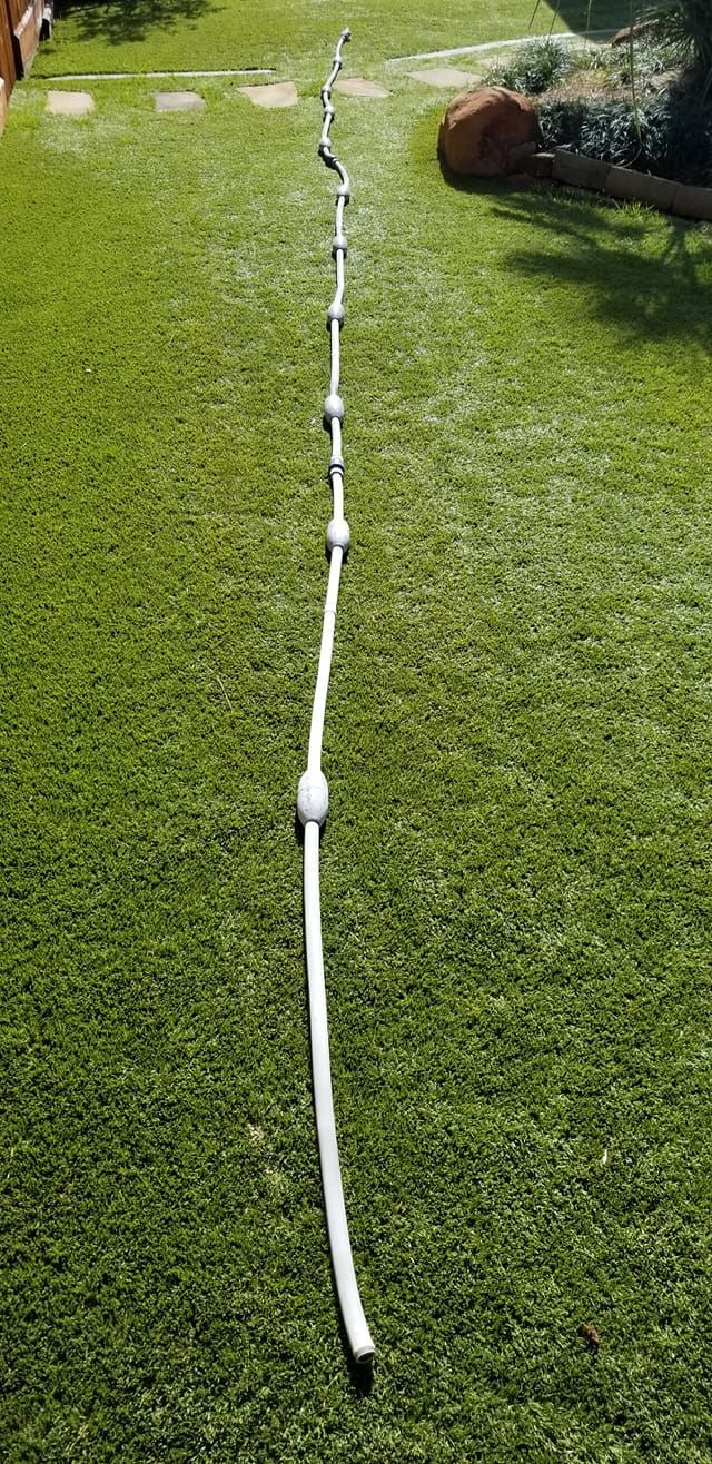 A long white hose is sitting on top of a lush green lawn.