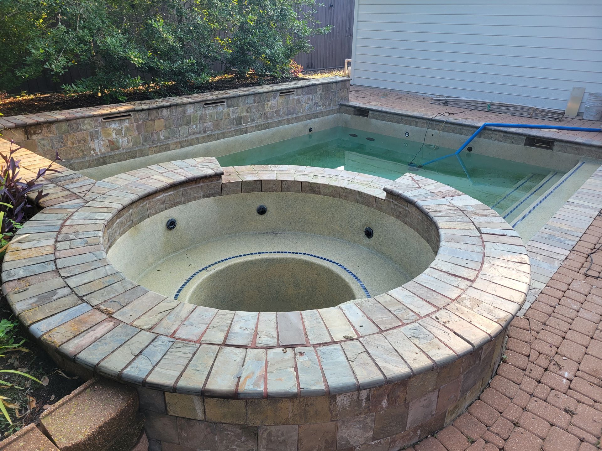 Two men are working on a swimming pool in a backyard.