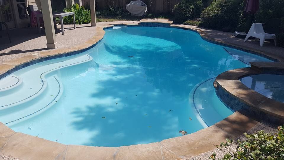 A large swimming pool with stairs and a patio in the backyard.