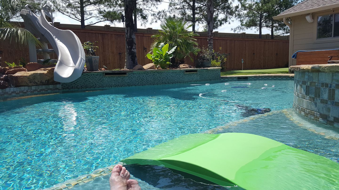 A person is laying on a green raft in a swimming pool.