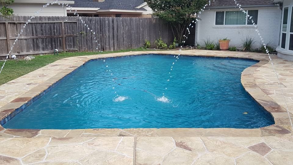 A large swimming pool with sprinklers in the backyard
