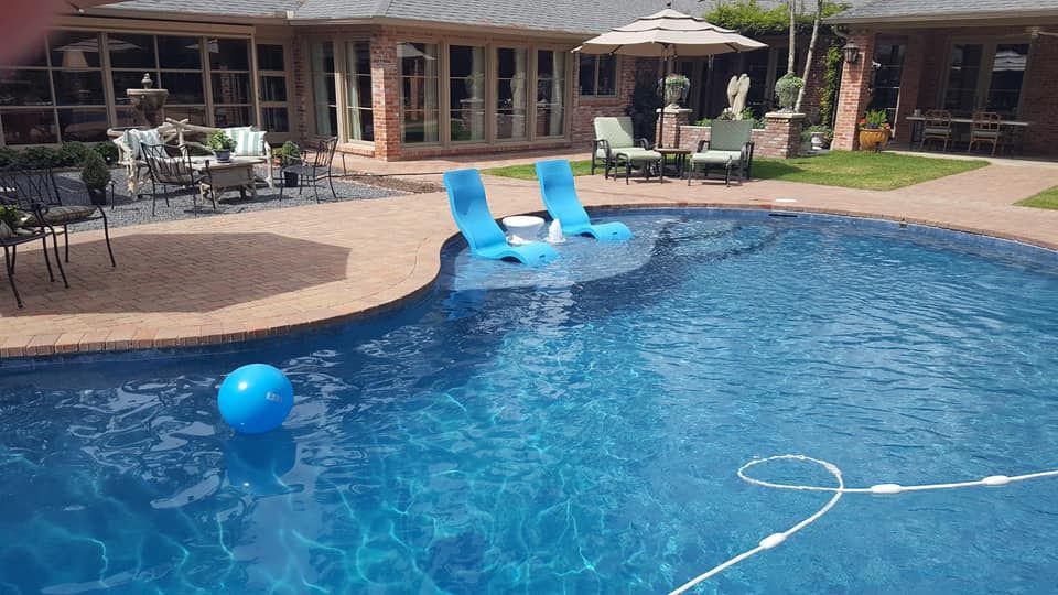 A large swimming pool with blue chairs and a blue ball in it.