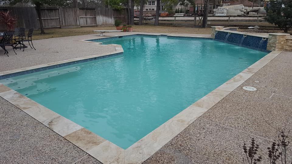 A large swimming pool with a waterfall in the backyard of a house.