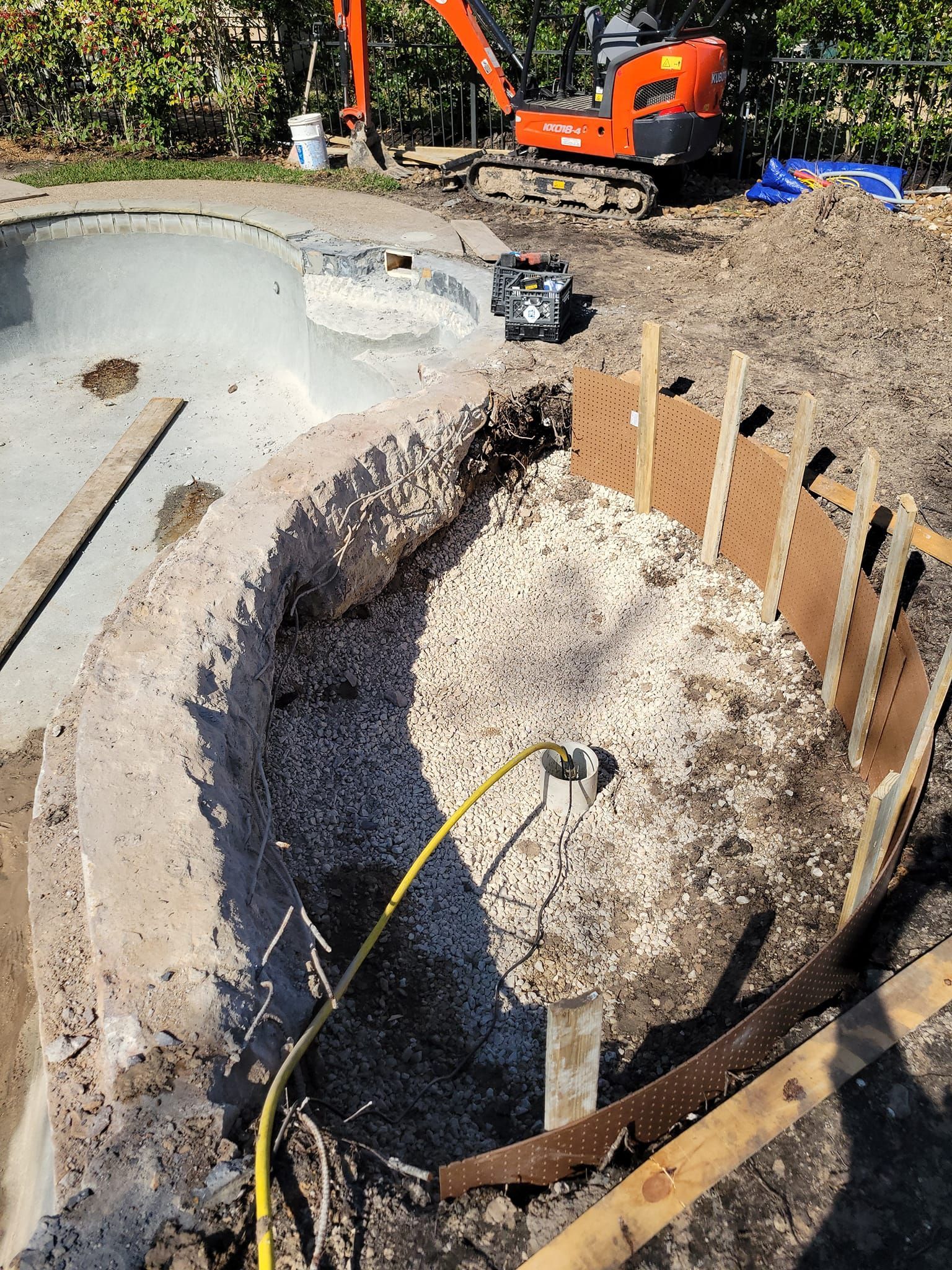 A large excavator is digging a hole in the ground next to a swimming pool.