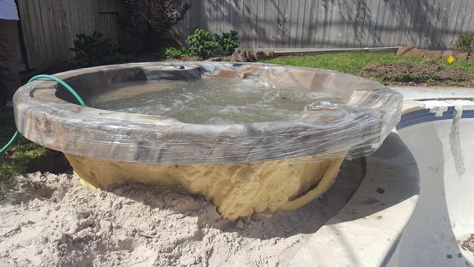 A hot tub is sitting in the sand next to a pool.
