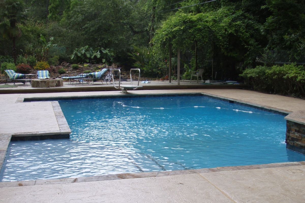 A large swimming pool surrounded by chairs and trees in a backyard.