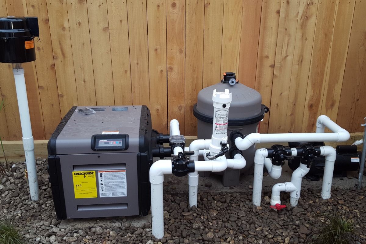 A swimming pool heater and filter are sitting next to a wooden fence.