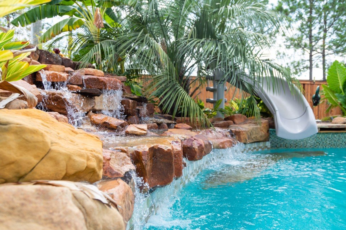 A swimming pool with a waterfall and a slide in the backyard.