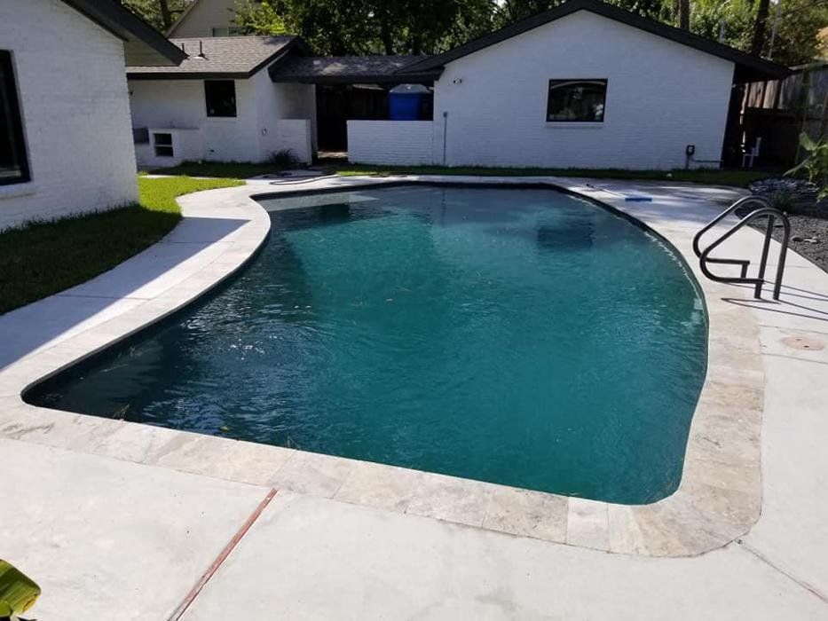 A large swimming pool is in the backyard of a house.