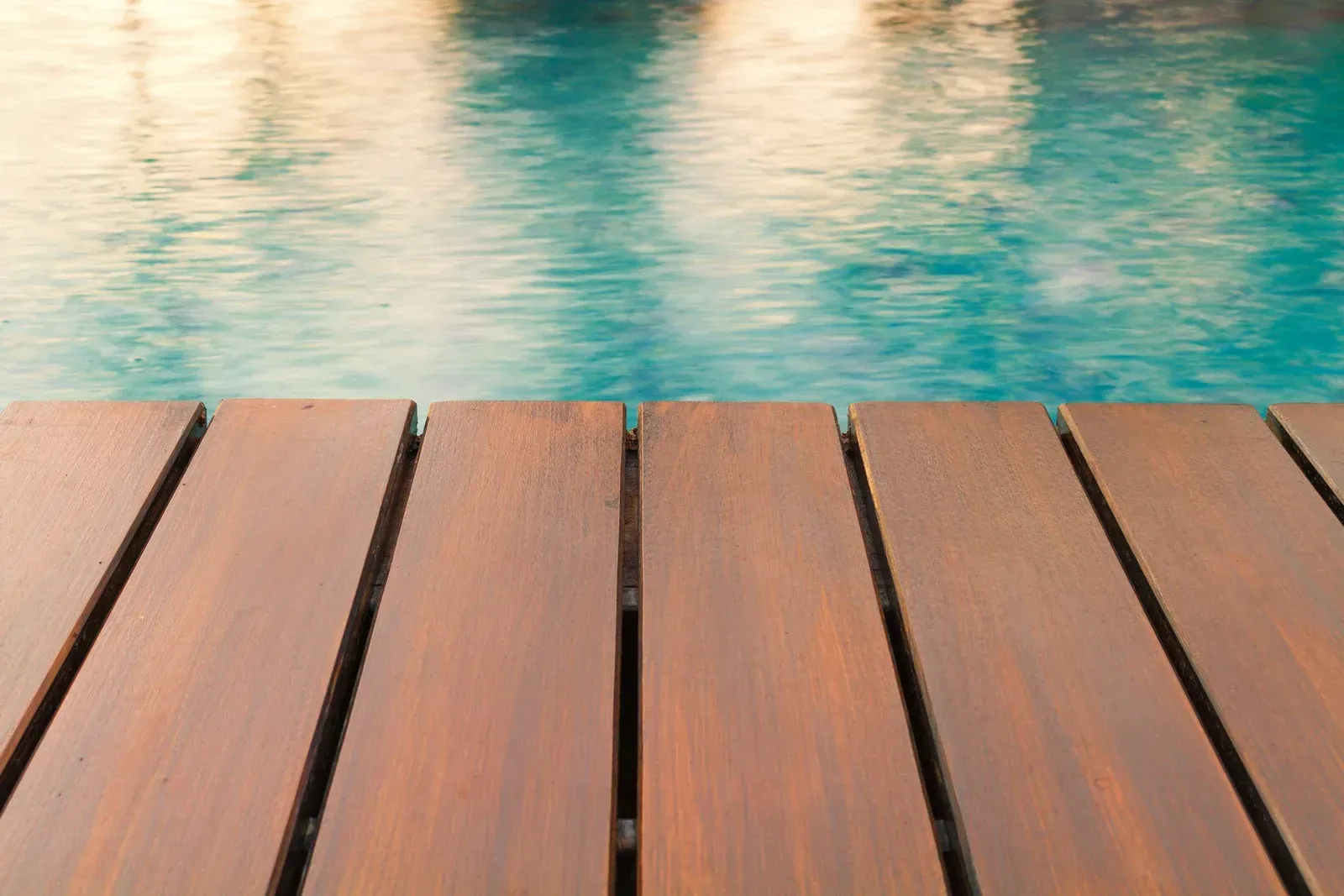 Wooden deck overlooking a turquoise pool; sunlight reflects on the water.