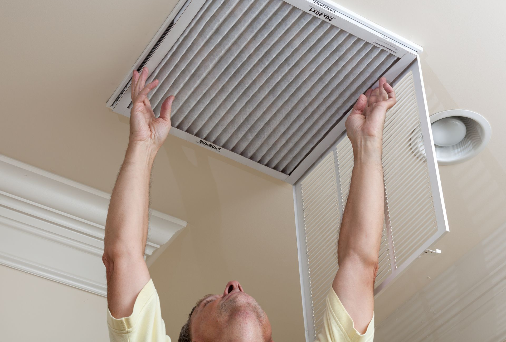Man opening ceiling air conditioning filter for home duct air care.