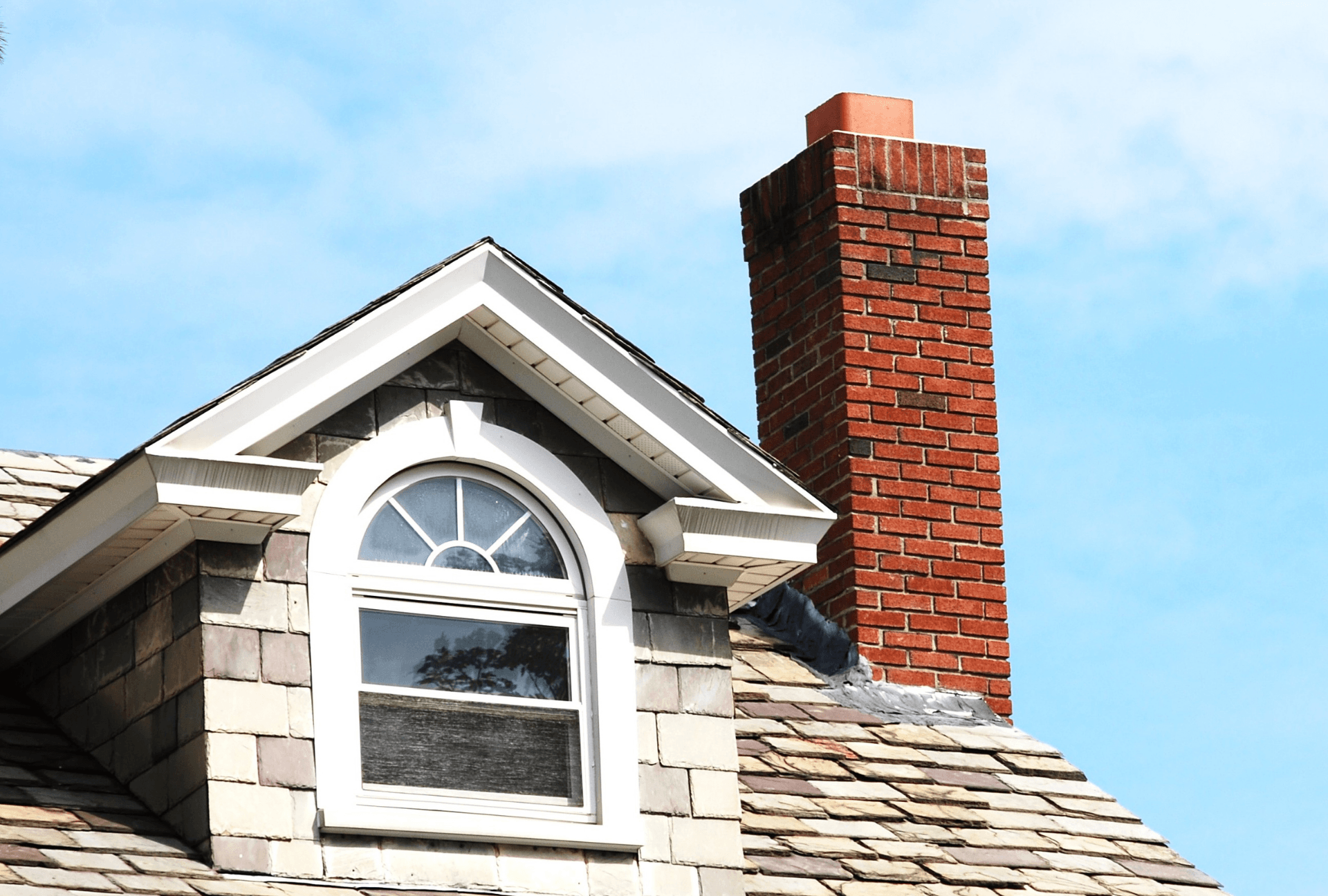 chimney repaired by ACE on the edge of a roof. Also show window, shingles, and a portion of the roof