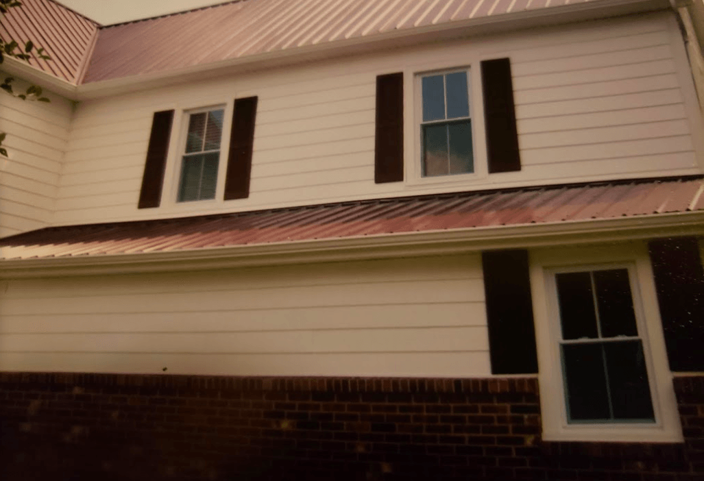 A white house with brown shutters and a red roof